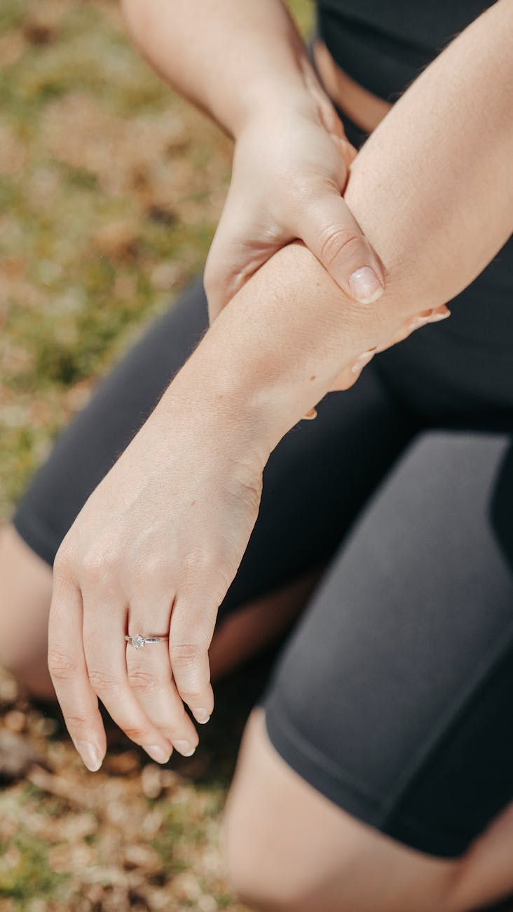 Close-up of a woman holding her wrist, indicating pain, while kneeling outdoors in athletic wear.